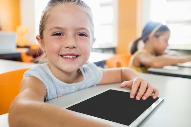 Jolie fille posant au bureau avec tablet pc en classe