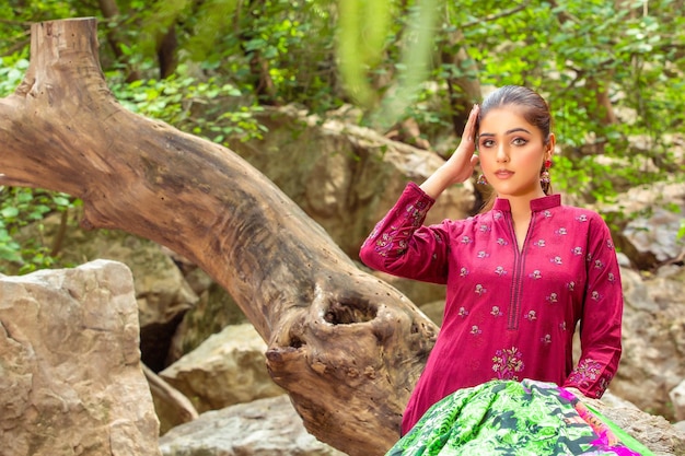 Jolie fille posant avec des racines d'arbres dans un parc à thème pour une séance de mode portant une robe rose traditionnelle