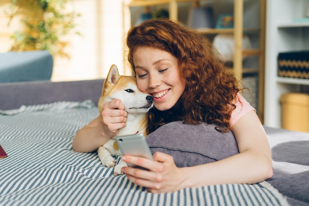 Jolie fille prenant silfie avec chiot à l'aide d'un appareil photo de smartphone allongé sur un canapé