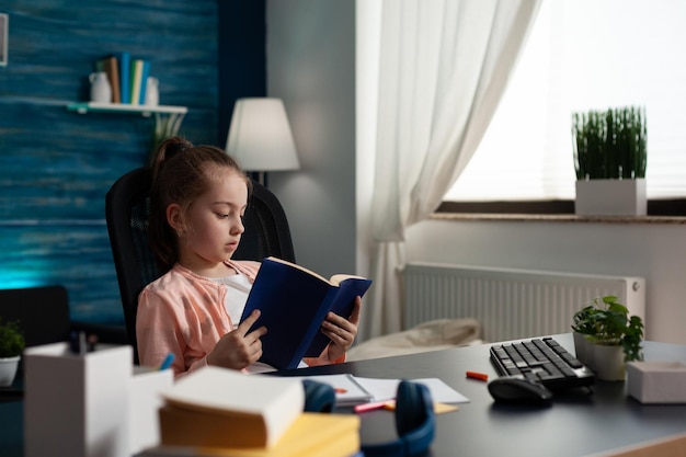 Une jolie fille qui lit un livre assise au bureau.