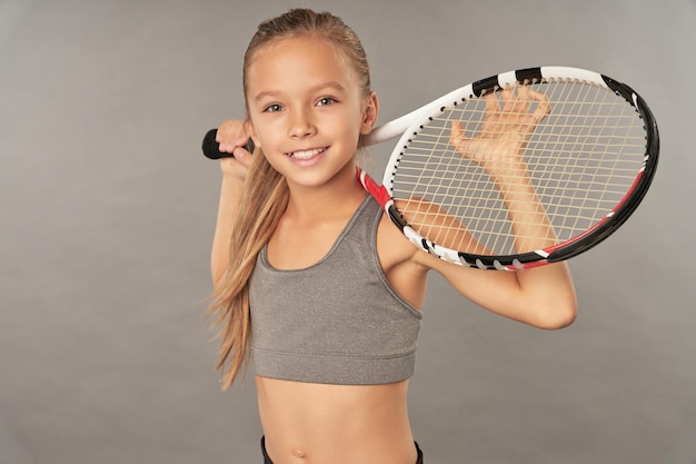 Jolie fille avec une raquette de tennis debout sur fond gris