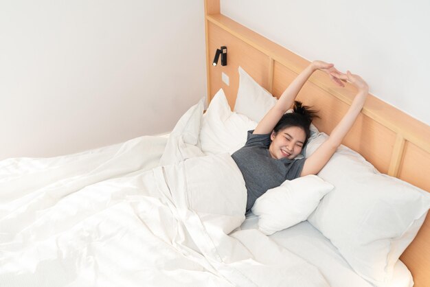 jolie fille à la recherche de bâillements endormis tout en étirant sa main sur le lit confortable blanc