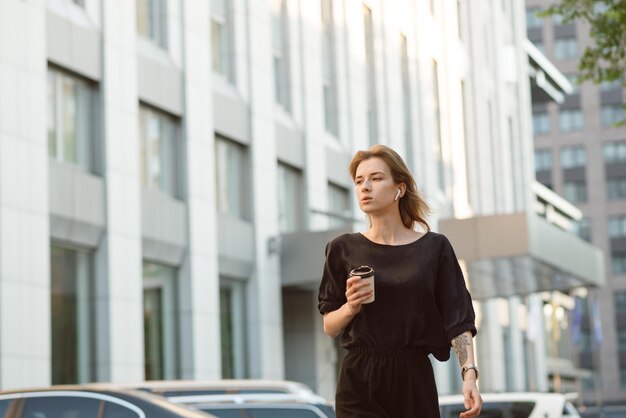 Jolie fille réfléchie marchant sur le centre-ville urbain avec une tasse de café par temps venteux