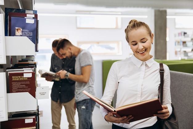 Photo jolie fille réfléchie ressemble à un étudiant debout avec un livre dans la bibliothèque d'une université