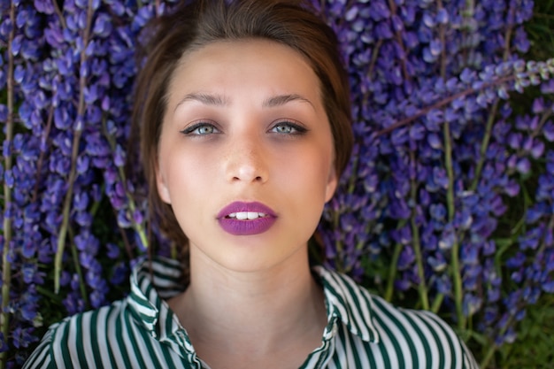 Jolie fille avec un regard sensuel à l'avant en fleurs de lupin violet