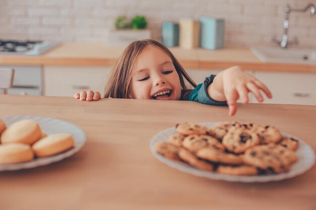 Jolie fille regardant de la table pour prendre le cookie de l'assiette