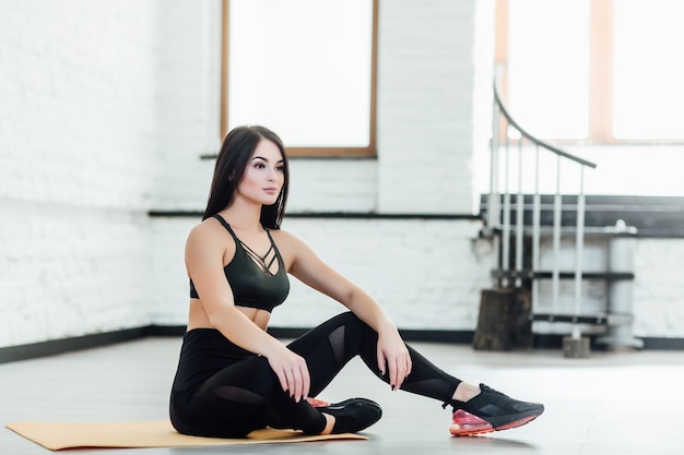 Jolie fille de remise en forme excitée dans le sportwear assis isolé sur blanc romm à la maison