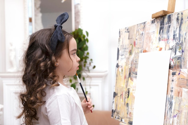 Une jolie fille rêveuse avec un pinceau près d'un chevalet de dessin un petit peintre