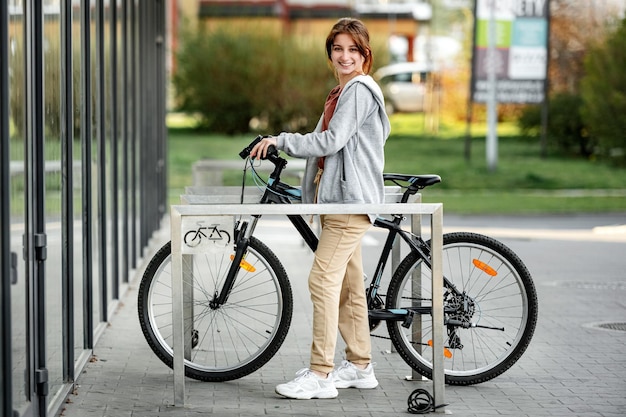Jolie fille riante garer un vélo sur un parking à vélo près du marché jeune fille souriante et regardant