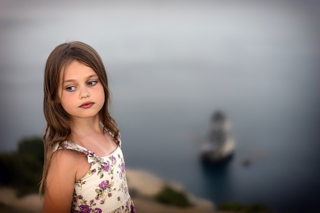 Jolie fille en robe d&#39;été avec les cheveux mouillés se dresse pensivement au bord de la mer.