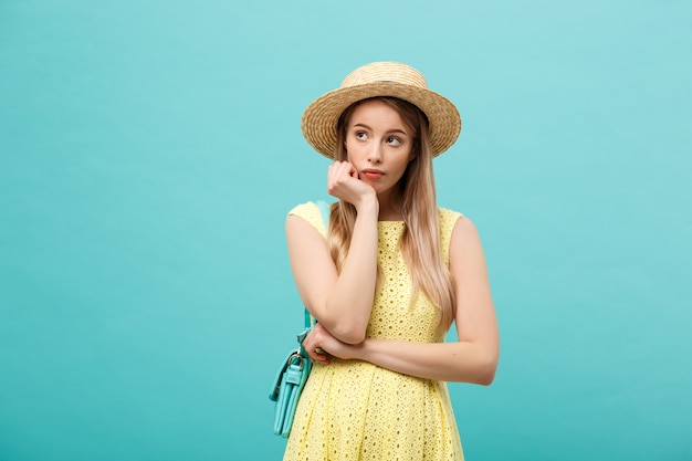 Jolie fille en robe d'été élégante sur fond bleu. Brunette au chapeau de paille pose pour la caméra.