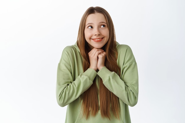 Jolie fille romantique, rêvant, regardant rêveuse dans le coin supérieur droit du fond, rêvant ou imaginant quelque chose avec un sourire tendre, debout sur un mur blanc