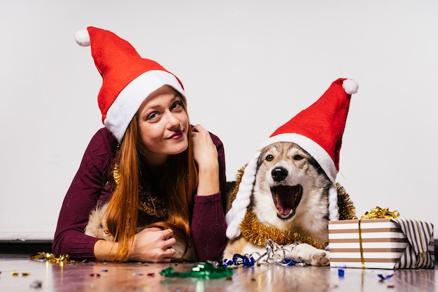 Jolie fille rousse avec un bonnet rouge sur la tête allongée sur le sol avec son chien, attendant la nouvelle année