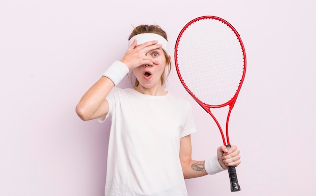 Jolie fille rousse qui a l'air choquée, effrayée ou terrifiée, couvrant le visage avec le concept de tennis à la main