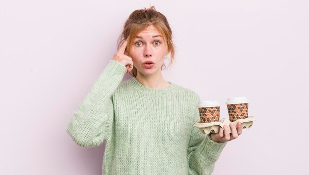 Jolie fille rousse qui a l'air surprise de réaliser une nouvelle idée ou un concept de pensée à emporter concept de café