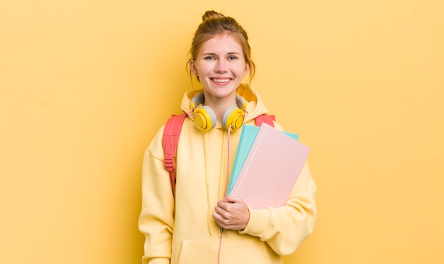 Jolie fille rousse souriant joyeusement avec une main sur la hanche et un concept d'étudiant confiant