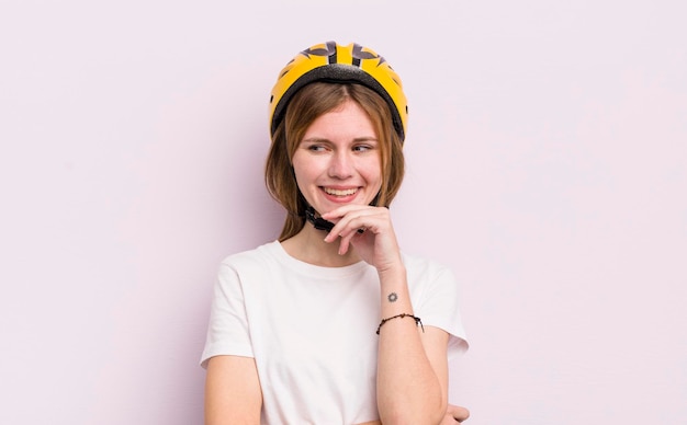 Jolie fille rousse souriante avec une expression confiante heureuse avec la main sur le concept de vélo de menton