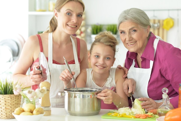 Jolie fille avec sa mère et sa grand-mère préparant une délicieuse salade fraîche dans la cuisine