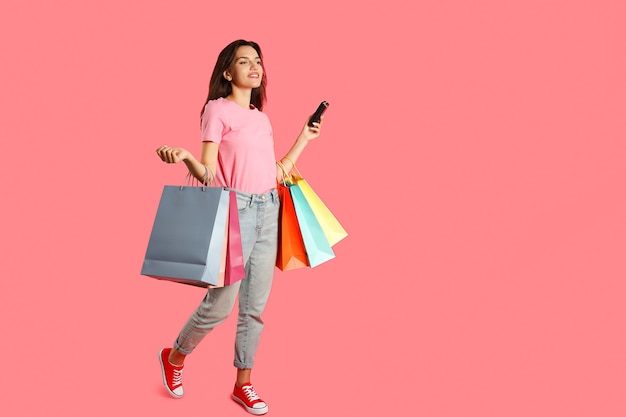 Jolie fille avec des sacs en papier multicolores sur fond rose.