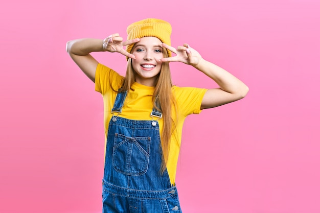 Une jolie fille en salopette en denim et un chapeau jaune sur rose