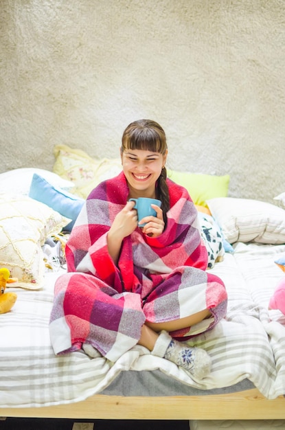 Jolie fille se prélassant sous une couverture avec une tasse de thé chaud