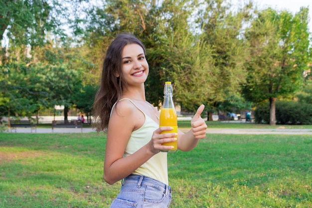 Jolie fille se promène dans le parc avec une bouteille de jus d&#39;orange dans une journée ensoleillée
