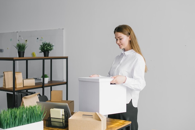 Une jolie fille se tient au bureau avec une grande boîte en papier blanc