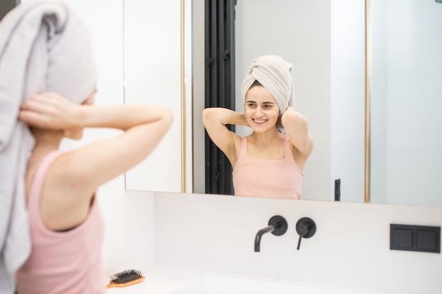Une jolie fille se tient dans la salle de bain avec une serviette sur la tête et fait de l'automassage