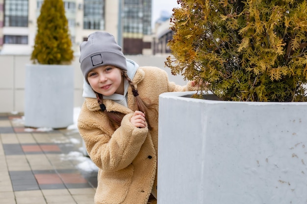 une jolie fille de sept ans jette un coup d'œil derrière un mur de béton joue à cache-cache