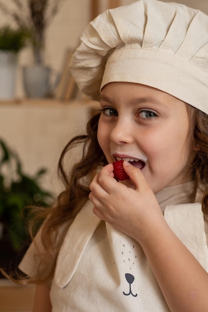 une jolie fille de six ans dans une toque de chef mange des framboises