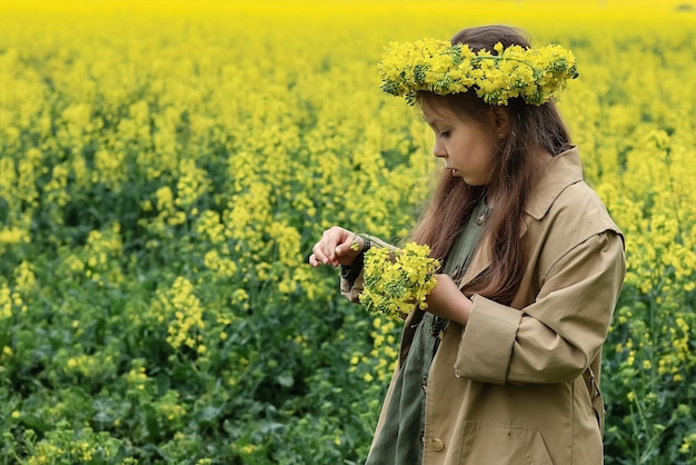 une jolie fille de six ans se tient dans un champ de colza avec une couronne de fleurs de colza sur la tête