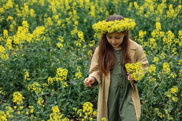 une jolie fille de six ans se tient dans un champ de colza et cueille un bouquet de fleurs dans le village