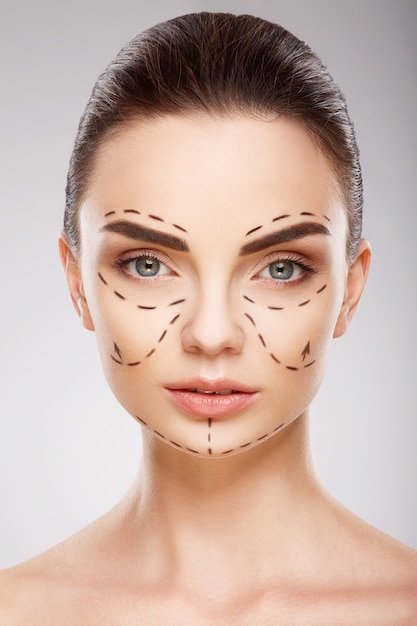 Jolie fille avec des sourcils sombres au mur avec des lignes de perforation sur le visage, concept de chirurgie plastique, gros plan portrait.