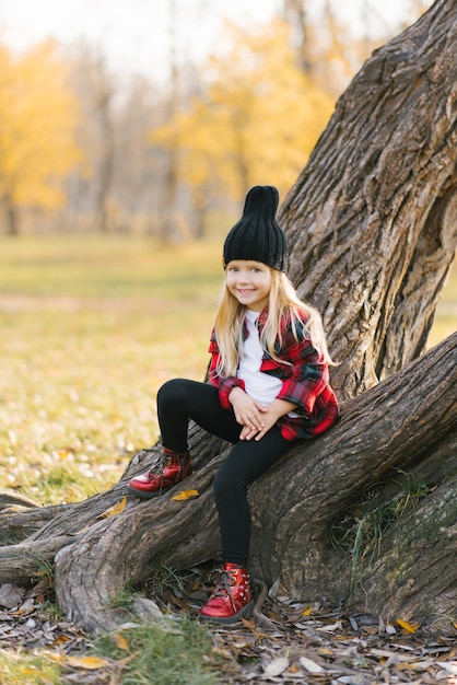 Jolie fille souriante assise sur un arbre dans la forêt d'automne