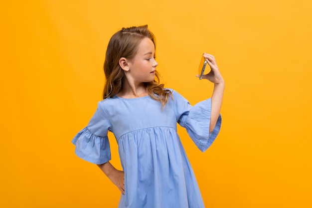 Jolie fille souriante dans une robe bleue en regardant une vidéo sur le téléphone en position horizontale sur jaune