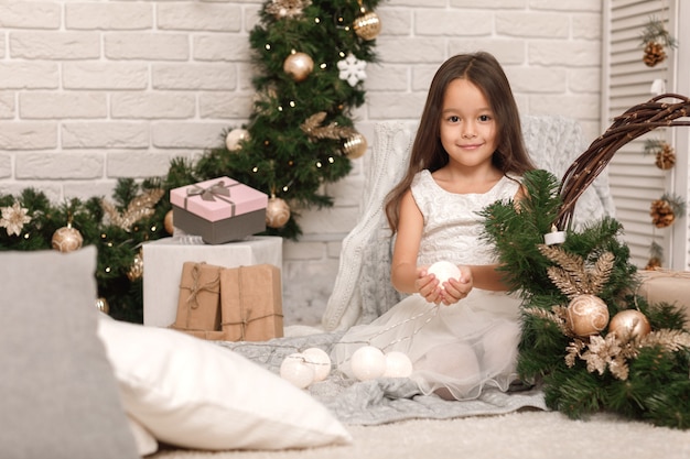 Jolie fille souriante décore le sapin de Noël à la maison