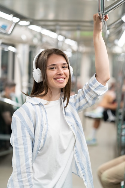 Une jolie fille souriante du millénaire écoutant de la musique avec des écouteurs sans fil dans une rame de métro