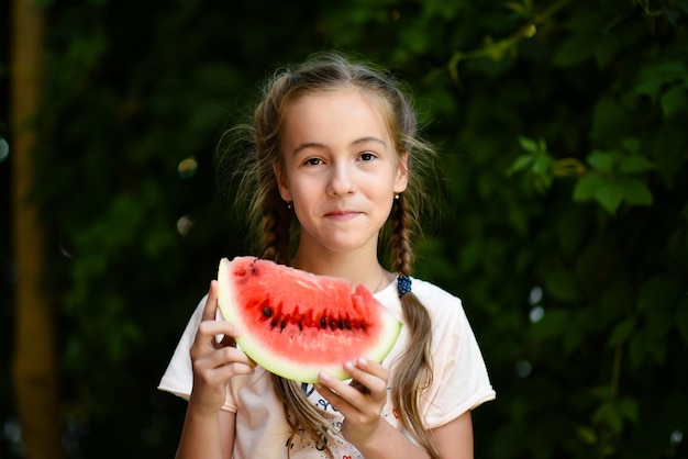 Une jolie fille souriante mange une pastèque rouge. Fond de feuilles vertes. La nature. Aliments. Été.