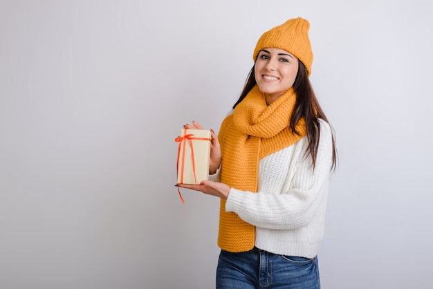 Jolie fille souriante tenant une boîte-cadeau et regardant la caméra sur fond gris