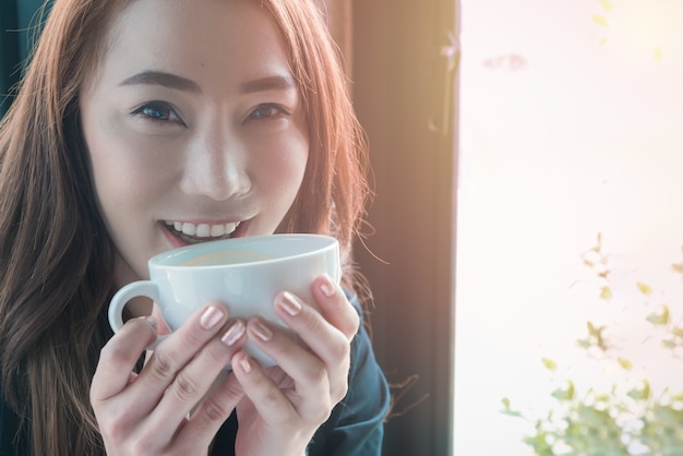 jolie fille sourire et sentir une tasse de café blanche