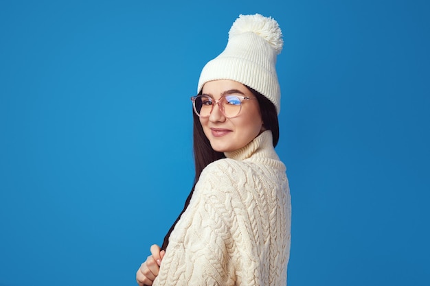 Jolie fille sourit à la caméra porte un chapeau blanc et un tricot blanc surdimensionné