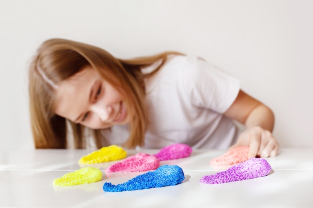 Une jolie fille sourit et regarde la boue multicolore allongée sur la table