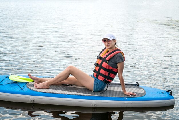 Jolie fille sportive apprendre à nager dans un gilet de sauvetage assis avec une pagaie sur une planche dans le style de vie d'été du lac de la ville