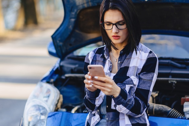 Jolie fille avec téléphone près du capot ouvert de la voiture