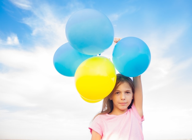 Jolie fille tenant des ballons de couleurs bleues et jaunes dans ses mains