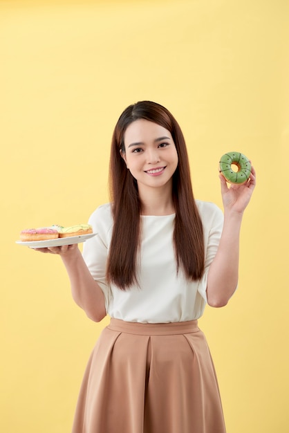 Jolie fille tenant des beignets frais et s'amusant avec des trucs sucrés. Bonne humeur, concept de régime.