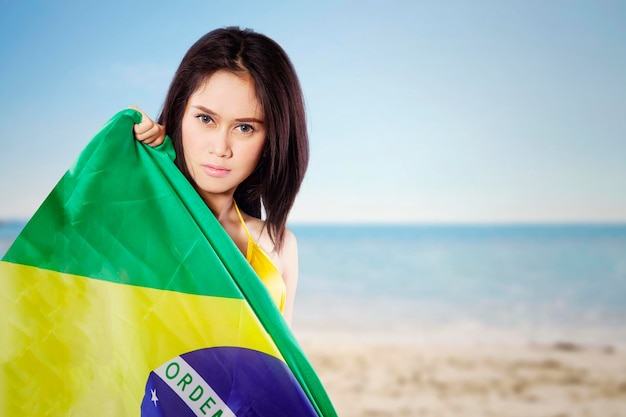 Jolie fille tenant le drapeau du Brésil sur la plage
