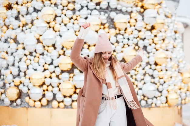 Photo jolie fille en tenue d'hiver élégante s'amusant devant l'arbre de noël à l'extérieur en hiver.