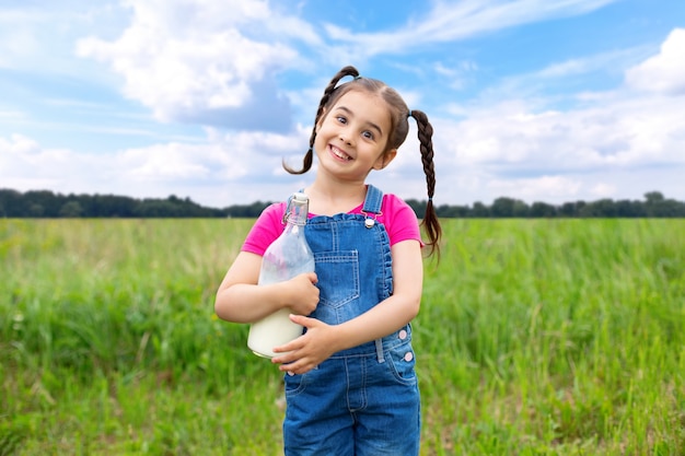 Jolie fille tient une bouteille de lait avec une paille rose, est assise sur une pelouse verte