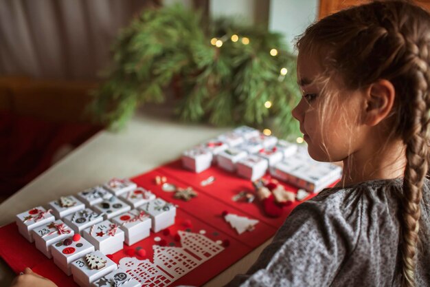 Une jolie fille tient un calendrier de l'avent original composé de boîtes à bijoux et d'un classeur de bricolage de noël